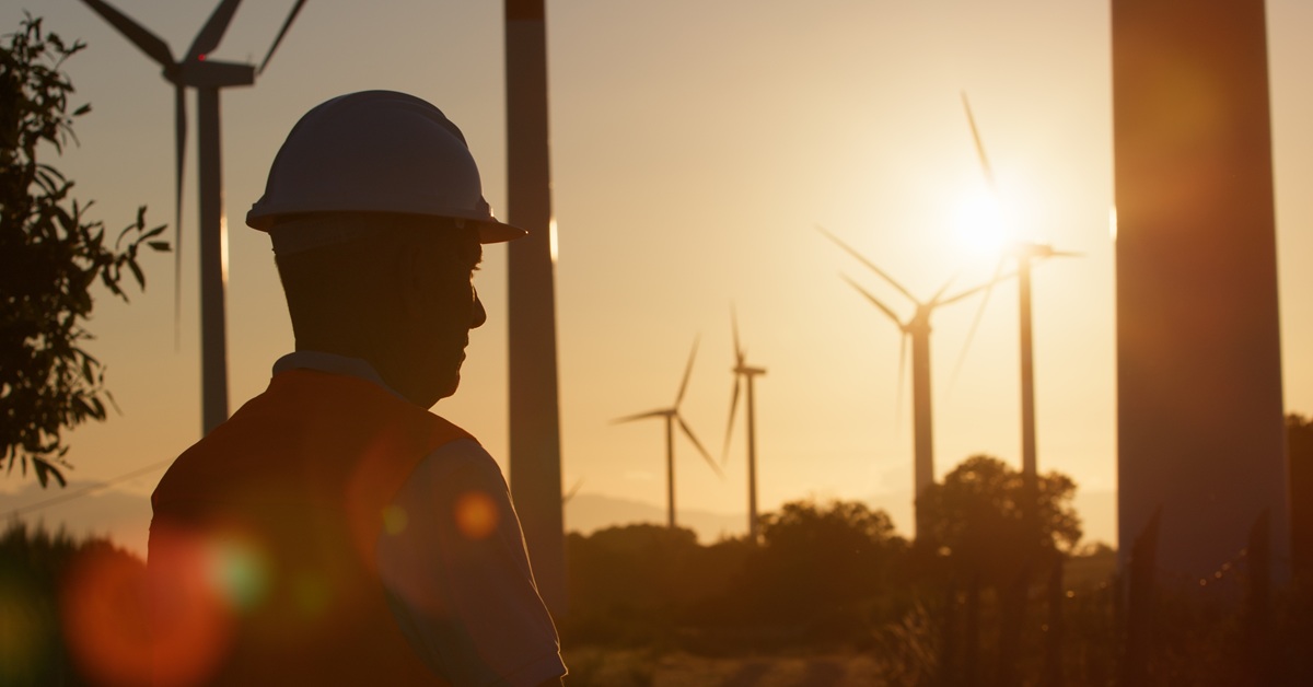 worker looking out at wind turbines during sunset