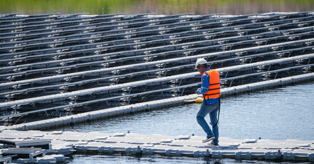 worker walking on floating solar panels on lake